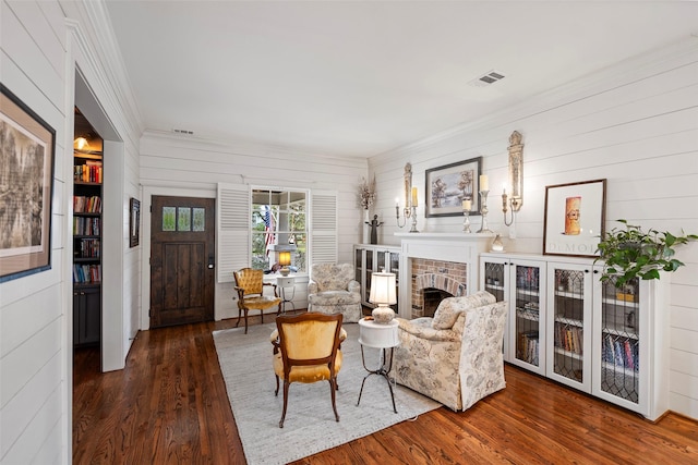 living area with a brick fireplace, dark wood-style floors, visible vents, and crown molding