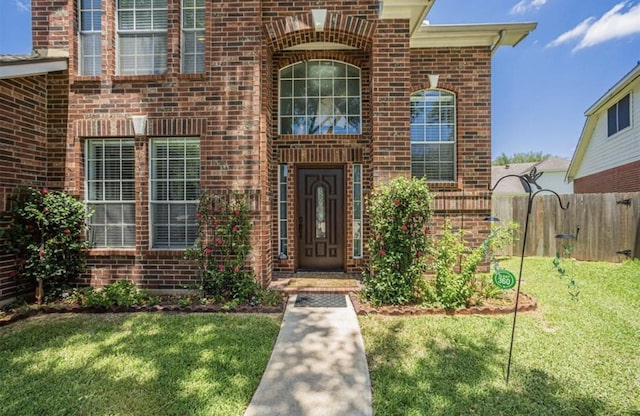 doorway to property with fence, a lawn, and brick siding