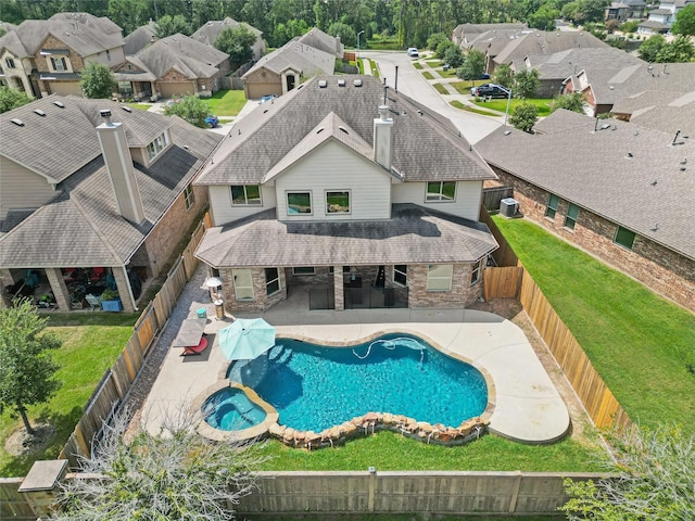 view of swimming pool featuring a fenced backyard, a pool with connected hot tub, a lawn, a residential view, and a patio area