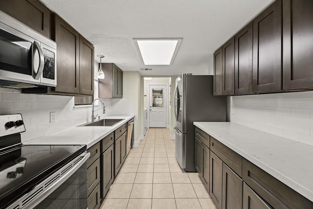 kitchen featuring stainless steel appliances, hanging light fixtures, backsplash, light tile patterned flooring, and a sink