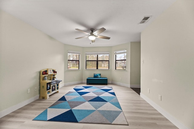 interior space with a ceiling fan, light wood-type flooring, visible vents, and baseboards