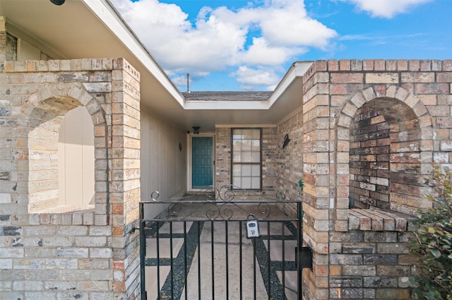 property entrance featuring a shingled roof, a gate, and brick siding