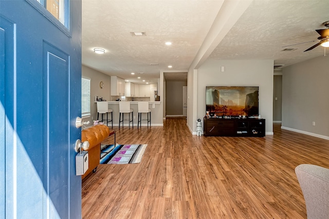 foyer featuring a textured ceiling, ceiling fan, visible vents, baseboards, and light wood finished floors