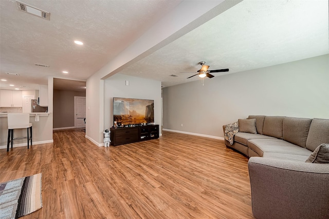 living area with a textured ceiling, baseboards, visible vents, and light wood-style floors