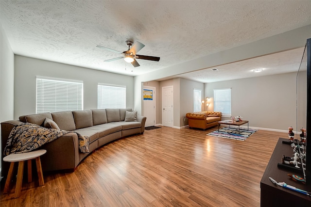 living room featuring ceiling fan, a textured ceiling, baseboards, and wood finished floors