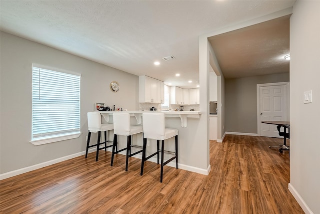 kitchen with light countertops, white cabinetry, wood finished floors, a peninsula, and a kitchen bar