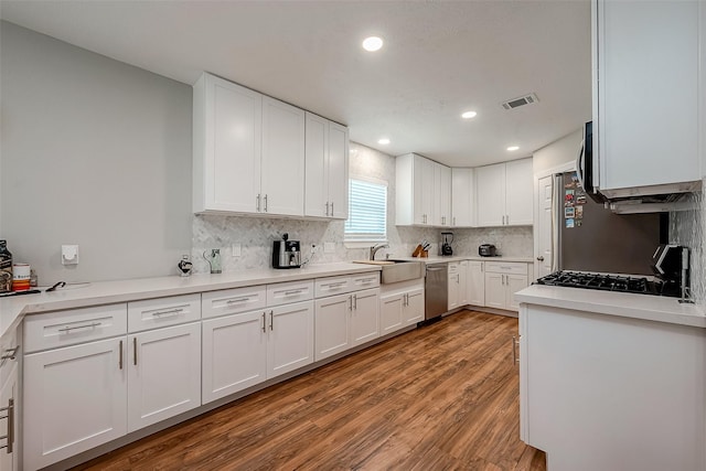 kitchen featuring light wood finished floors, white cabinets, appliances with stainless steel finishes, light countertops, and a sink