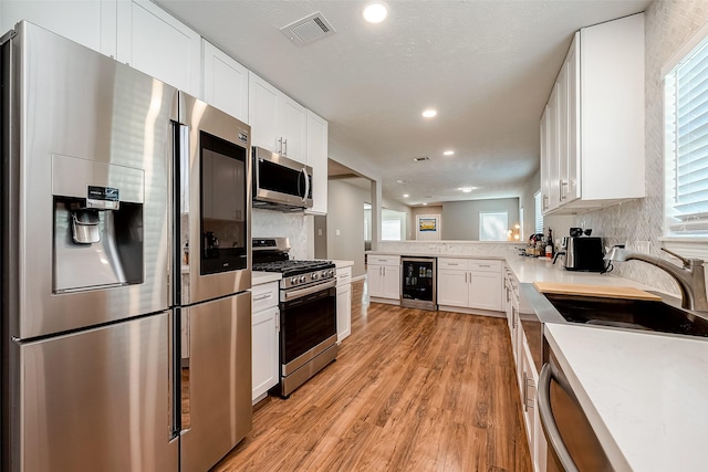 kitchen featuring stainless steel appliances, wine cooler, light countertops, and visible vents