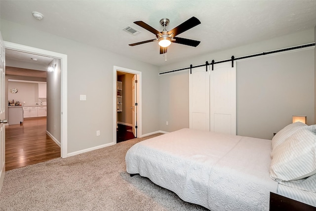 bedroom featuring carpet, visible vents, a barn door, a ceiling fan, and baseboards