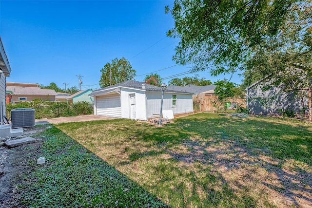 view of yard with a detached garage, fence, central AC, and an outbuilding