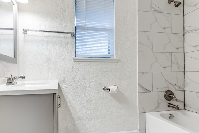 bathroom with a textured wall, tub / shower combination, and vanity