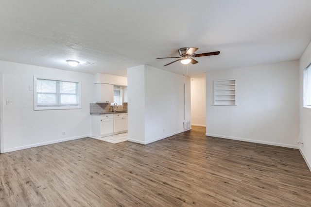 unfurnished living room with built in features, baseboards, ceiling fan, wood finished floors, and a sink