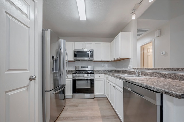 kitchen featuring stainless steel appliances, dark countertops, a sink, and white cabinets