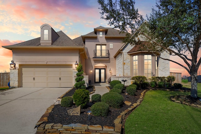 french country style house featuring driveway, an attached garage, a balcony, and stucco siding