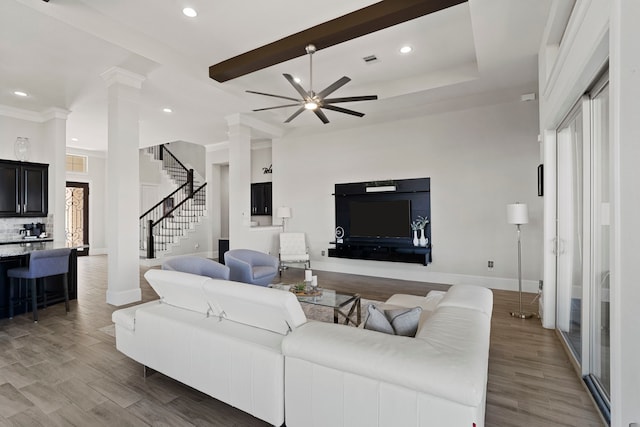 living area featuring light wood-type flooring, decorative columns, stairway, and ceiling fan