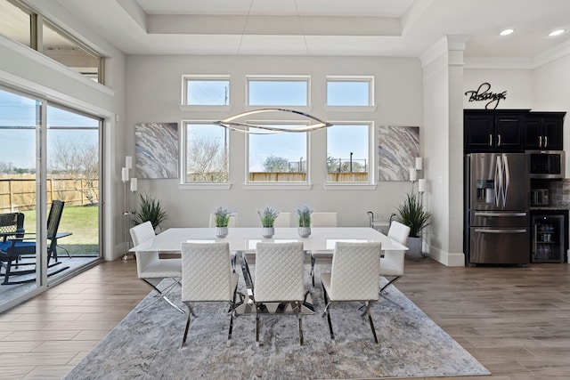 dining space featuring a tray ceiling, beverage cooler, baseboards, and wood finished floors