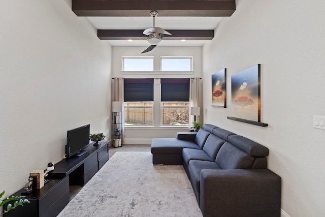 living area featuring a healthy amount of sunlight, beamed ceiling, baseboards, and ceiling fan