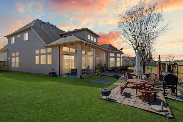 back of house at dusk featuring a patio, a yard, a fenced backyard, and a sunroom