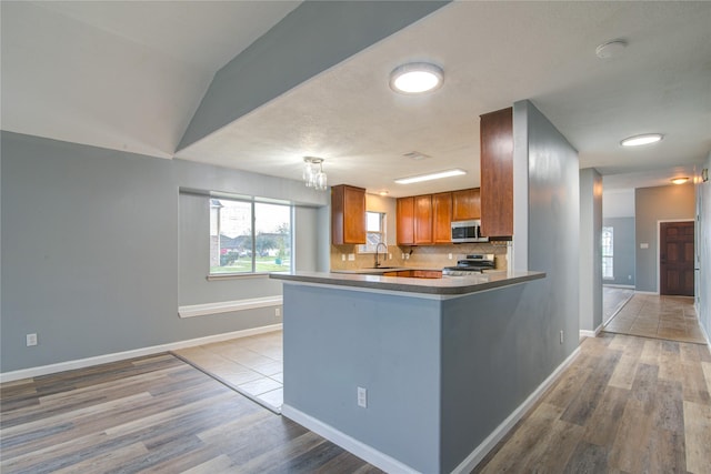 kitchen featuring stainless steel appliances, dark countertops, tasteful backsplash, brown cabinetry, and a sink