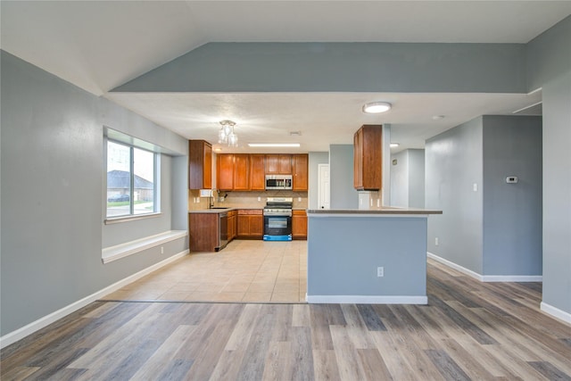 kitchen with a sink, light countertops, appliances with stainless steel finishes, light wood-type flooring, and brown cabinets