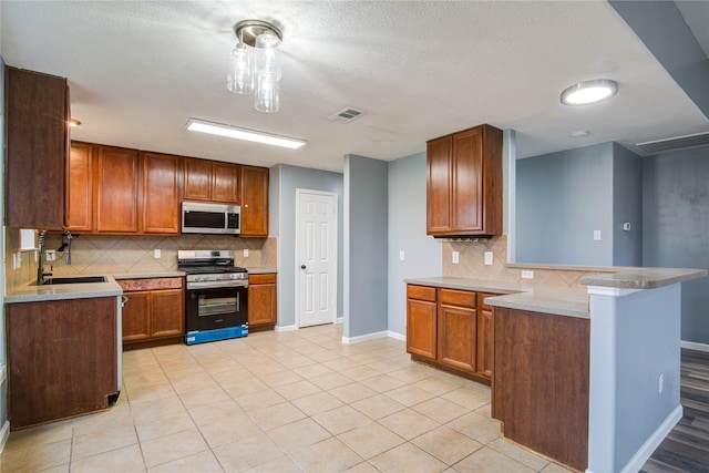 kitchen with a peninsula, a sink, light countertops, appliances with stainless steel finishes, and brown cabinetry