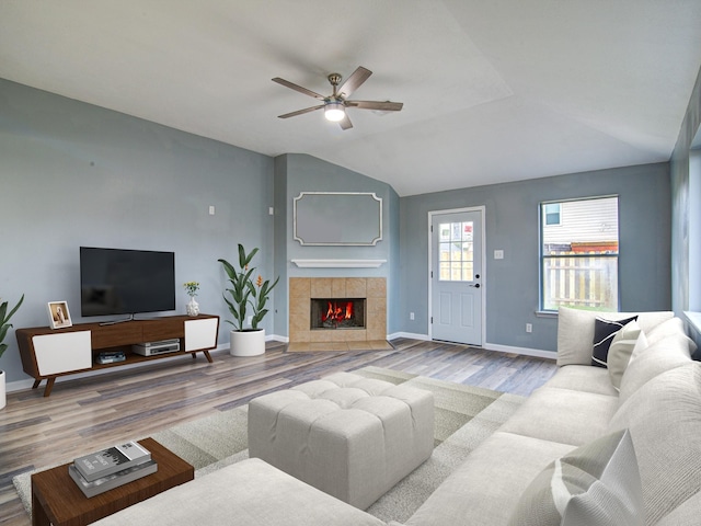 living area with lofted ceiling, baseboards, a tiled fireplace, and wood finished floors