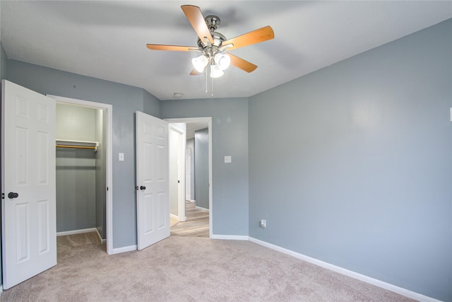 unfurnished bedroom featuring a walk in closet, a closet, light colored carpet, a ceiling fan, and baseboards