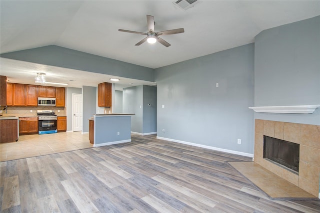 unfurnished living room with a tile fireplace, a ceiling fan, visible vents, baseboards, and light wood-type flooring