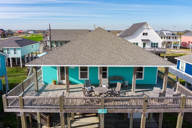 back of house featuring a shingled roof, outdoor dining area, a wooden deck, and a residential view