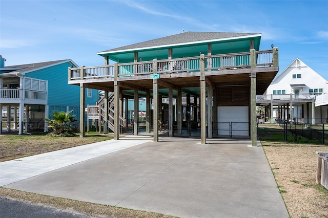 coastal home featuring roof with shingles, stairway, a carport, and concrete driveway