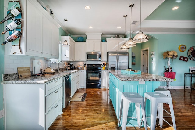 kitchen with white cabinets, a kitchen island, decorative light fixtures, stainless steel appliances, and a sink