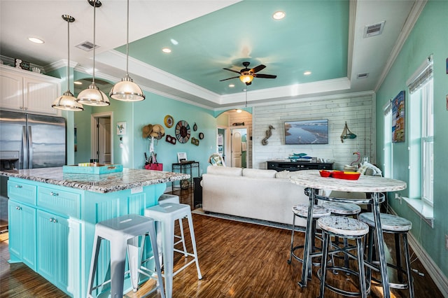 kitchen with arched walkways, a kitchen island, visible vents, a raised ceiling, and pendant lighting