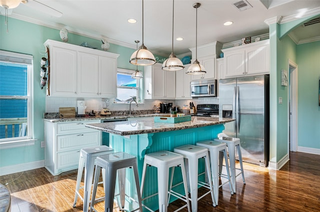 kitchen featuring white cabinetry, appliances with stainless steel finishes, a center island, dark stone counters, and decorative light fixtures