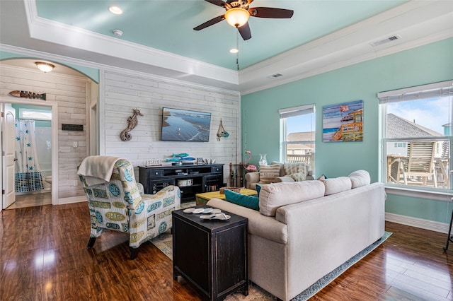 living area featuring visible vents, a tray ceiling, arched walkways, and dark wood-type flooring