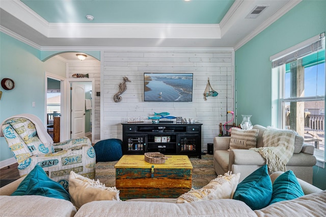 living area with visible vents, arched walkways, a raised ceiling, and ornamental molding