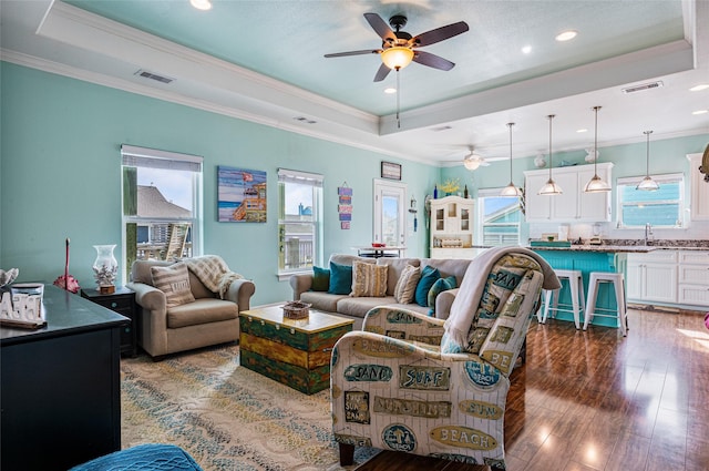 living room featuring ornamental molding, a tray ceiling, dark wood-style flooring, and visible vents