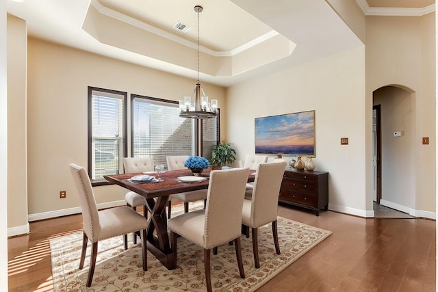 dining space featuring visible vents, arched walkways, wood finished floors, a tray ceiling, and a notable chandelier