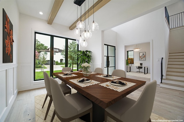 dining area with light wood finished floors, stairway, a decorative wall, and beam ceiling