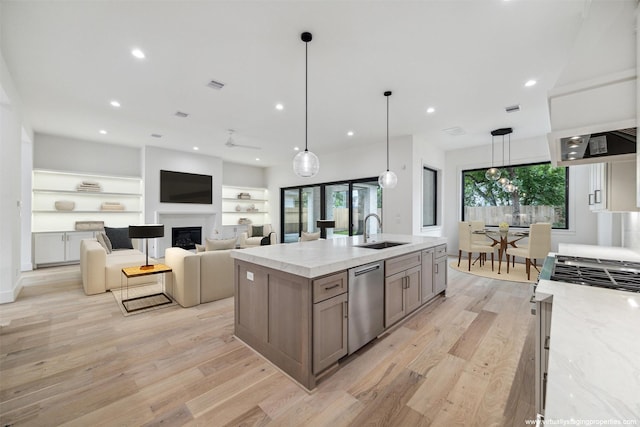 kitchen featuring appliances with stainless steel finishes, light stone counters, light wood-type flooring, a fireplace, and a sink