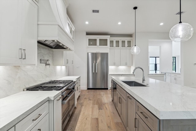 kitchen featuring stainless steel appliances, a sink, visible vents, glass insert cabinets, and custom range hood