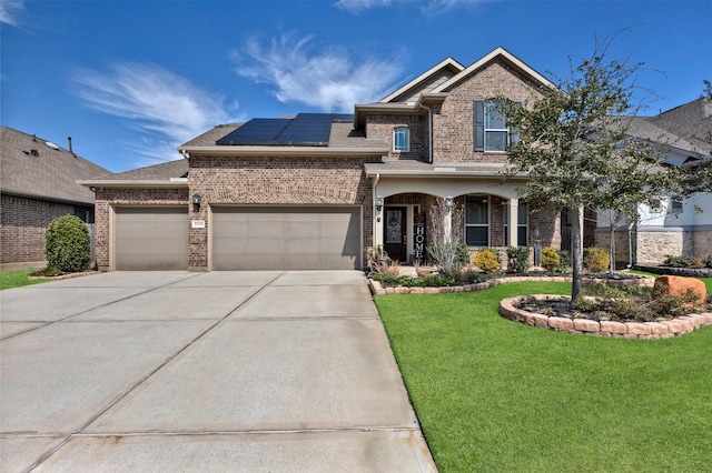 view of front of house with a garage, brick siding, roof mounted solar panels, and a front yard