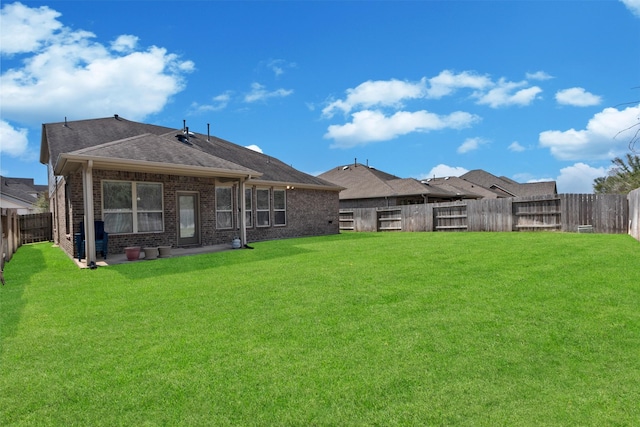 rear view of house featuring a yard, brick siding, roof with shingles, and a fenced backyard