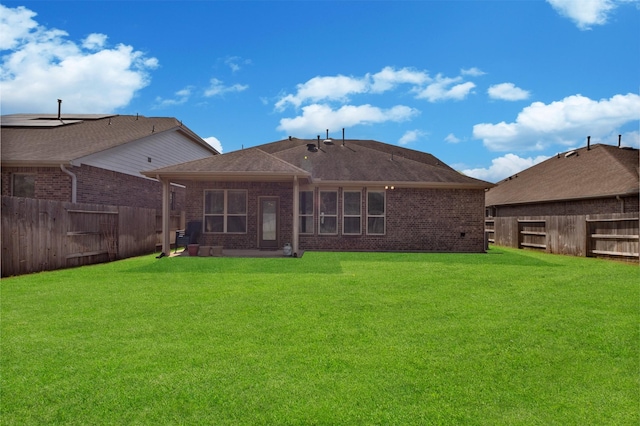 back of property with brick siding, a fenced backyard, and a yard