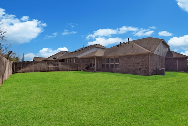 rear view of property with central air condition unit, a fenced backyard, a lawn, and brick siding