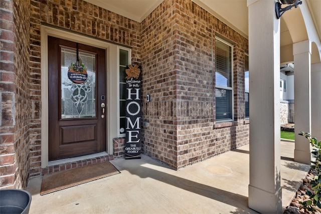 view of exterior entry featuring a porch and brick siding