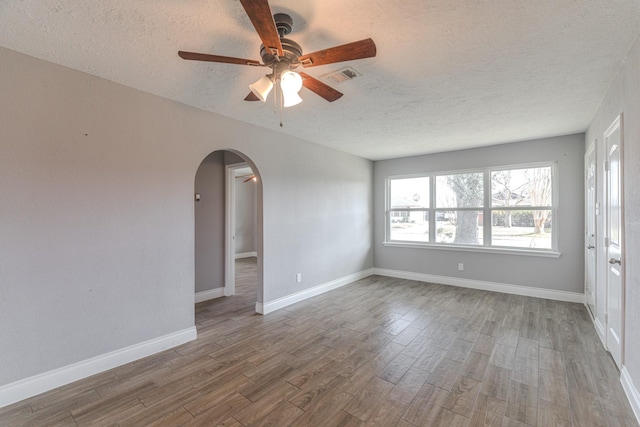 unfurnished room featuring baseboards, visible vents, arched walkways, wood finished floors, and a textured ceiling