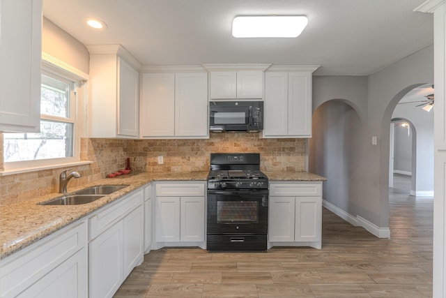 kitchen featuring arched walkways, white cabinetry, a sink, light stone countertops, and black appliances