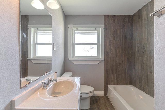 bathroom with toilet, baseboards, a wealth of natural light, and wood finished floors