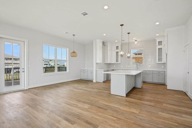26726 Estuary Dr, Galveston, TX 77554 - kitchen with white cabinets, a kitchen island, glass insert cabinets, hanging light fixtures, and light countertops