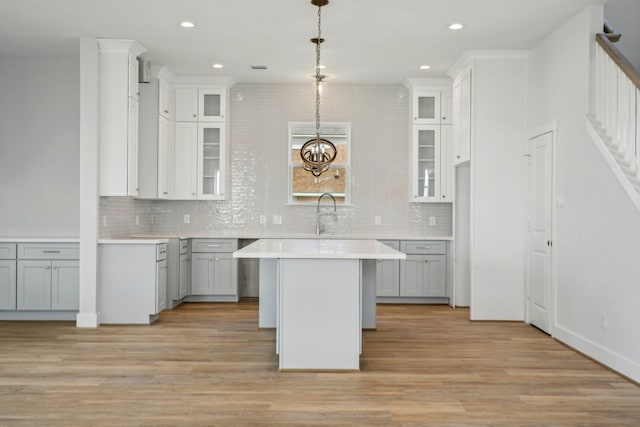 26726 Estuary Dr, Galveston, TX 77554 - kitchen with glass insert cabinets, decorative light fixtures, a center island, light countertops, and light wood-type flooring
